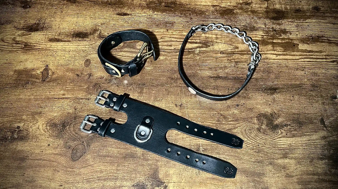 Handcrafted black leather cuffs, collar, and harness on a wooden studio bench showcasing traditional craftsmanship.