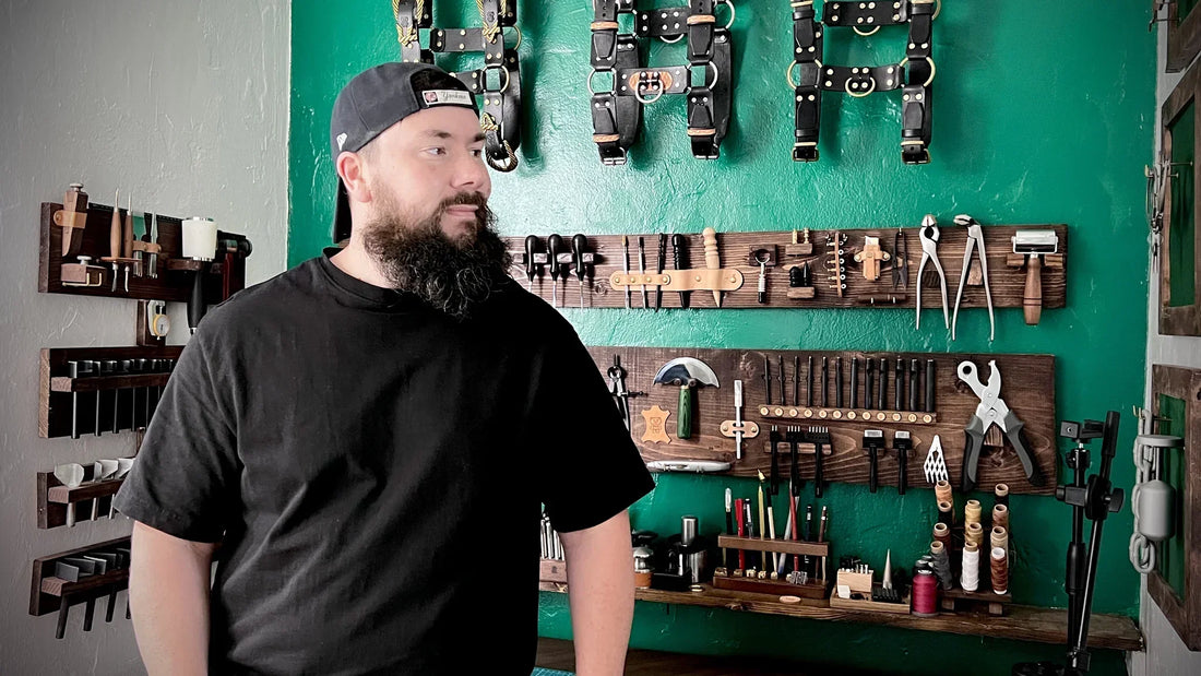 A leathercraft artisan standing inside a workshop filled with structured wall-mounted tool racks and hanging gear.