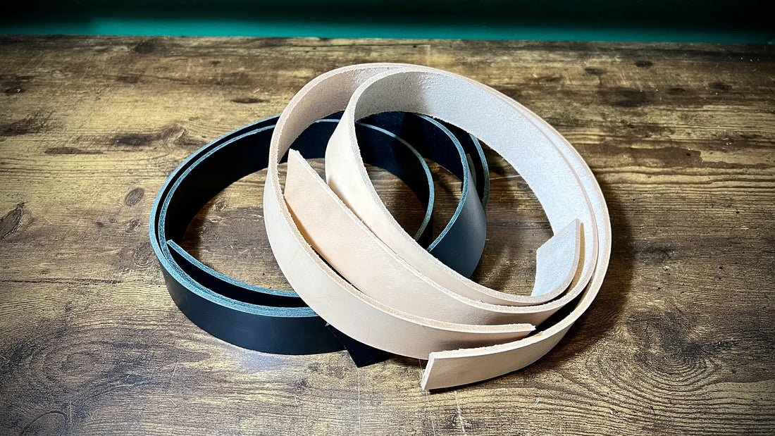 Coils of raw natural and dyed black vegetable-tanned leather straps ready for bench-crafting on a dark wood surface