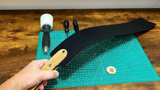 Handcrafted black leather spanking implement on green cutting mat showing a carved wooden handle and burnished edges.