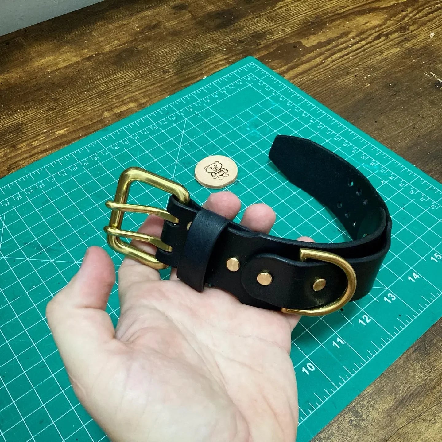 Close-up of a double-buckle black leather strap layout showing solid brass hardware rivets and matching D-rings.