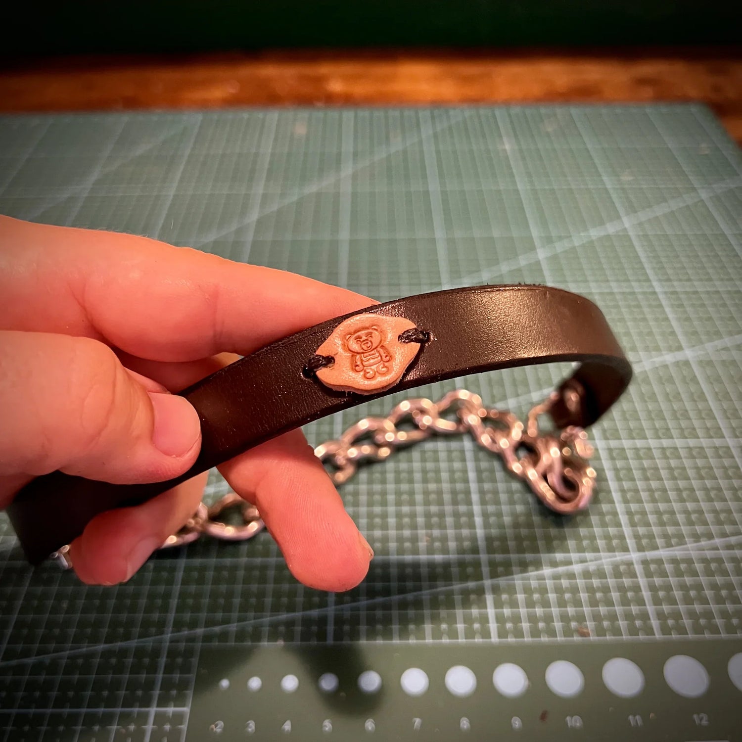 Handcrafted black leather collar with an embossed logo medallion spliced onto high-tensile steel chain links.