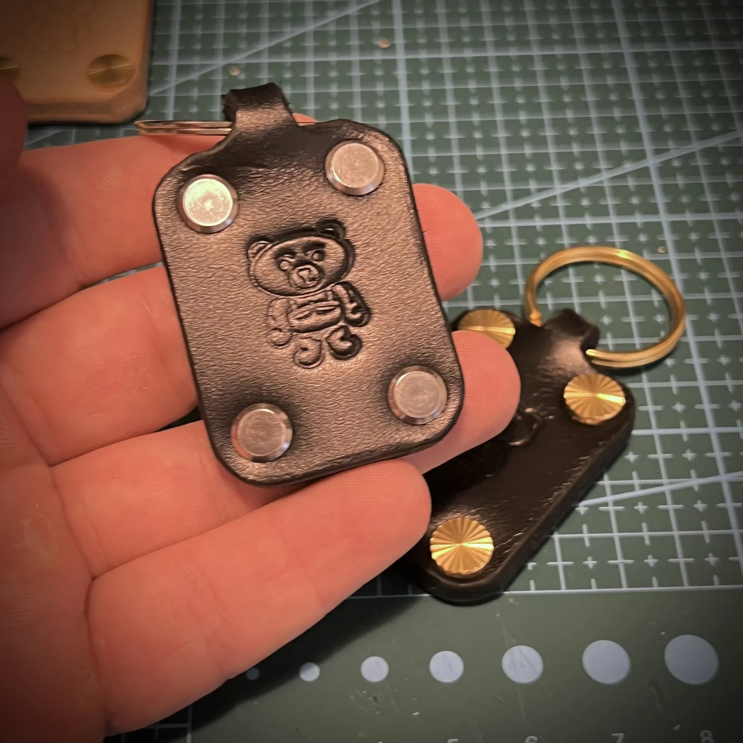 Close-up of a black leather bear keychain held by an artisan, highlighting clean edge burnishing and hardware.