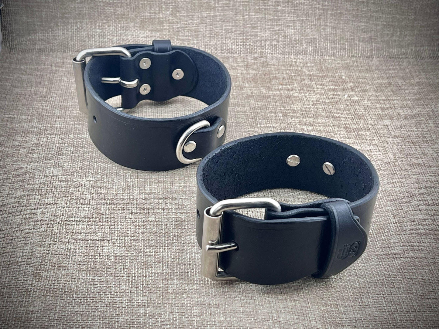 Two black leather cuffs with metal buckles on a textured gray background
