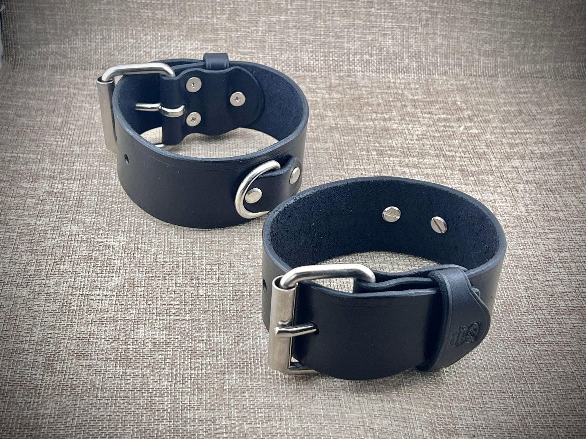 Two black leather cuffs with metal buckles on a textured gray background