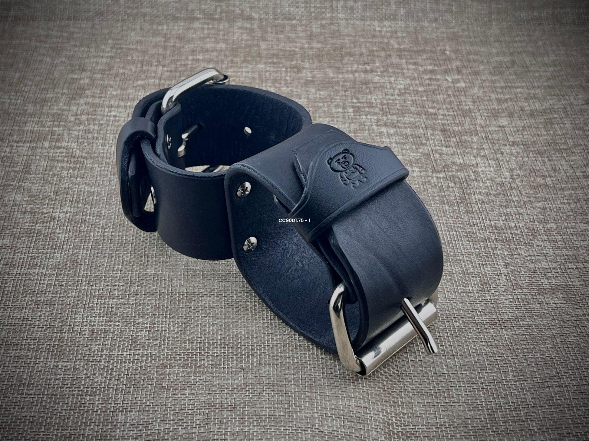 Black leather straps with metal buckle on a textured gray background