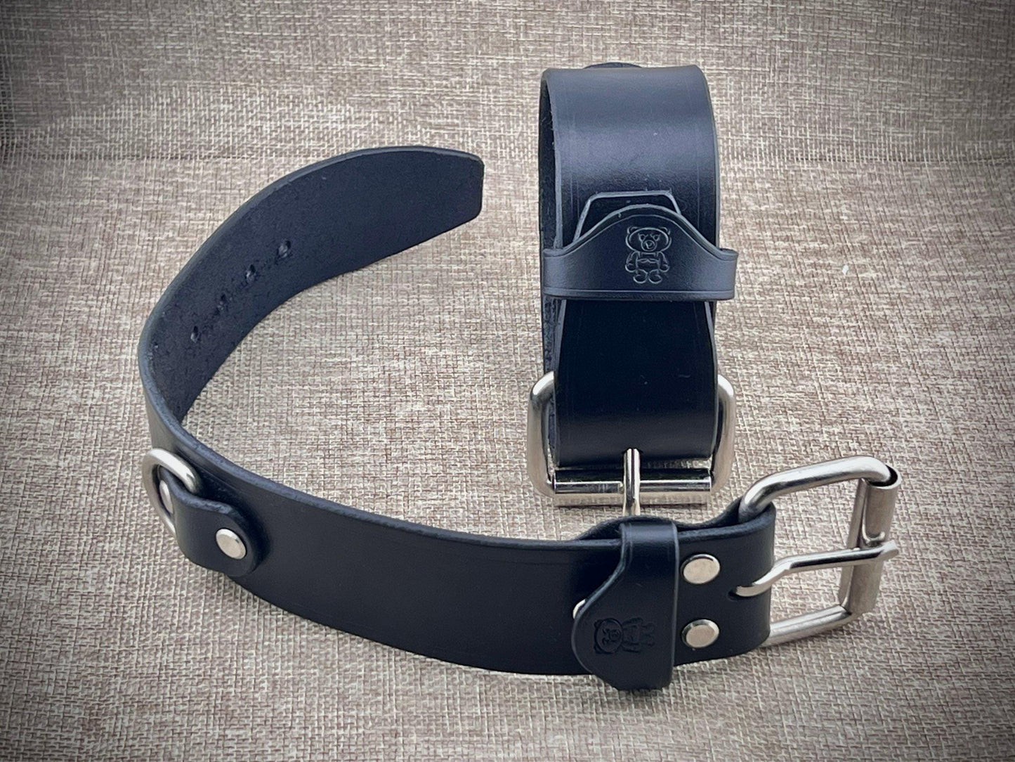 Two black leather cuffs with metal buckles on a textured gray background
