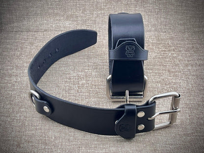 Two black leather cuffs with metal buckles on a textured gray background