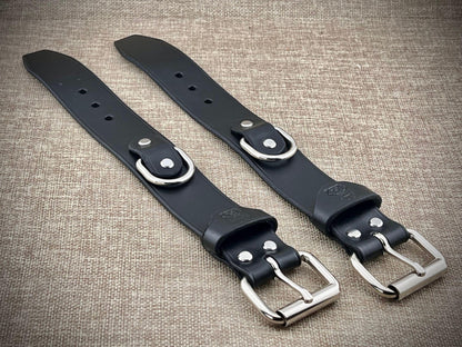Two black leather straps with silver buckles on a textured brown background