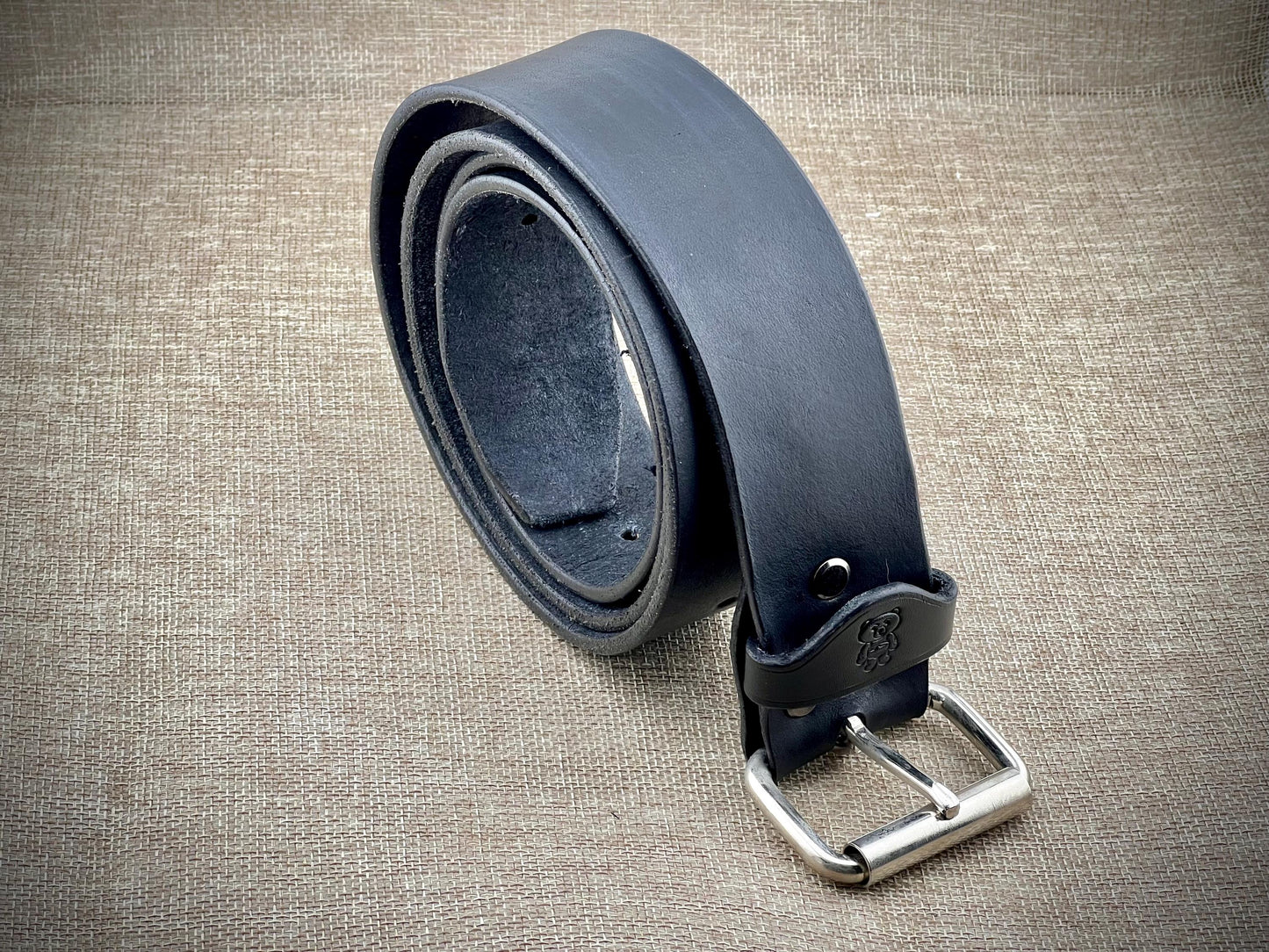 Black leather belt with steel buckle on a textured beige surface
