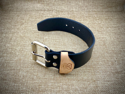 Black leather cuff with a metal buckle on a textured beige background