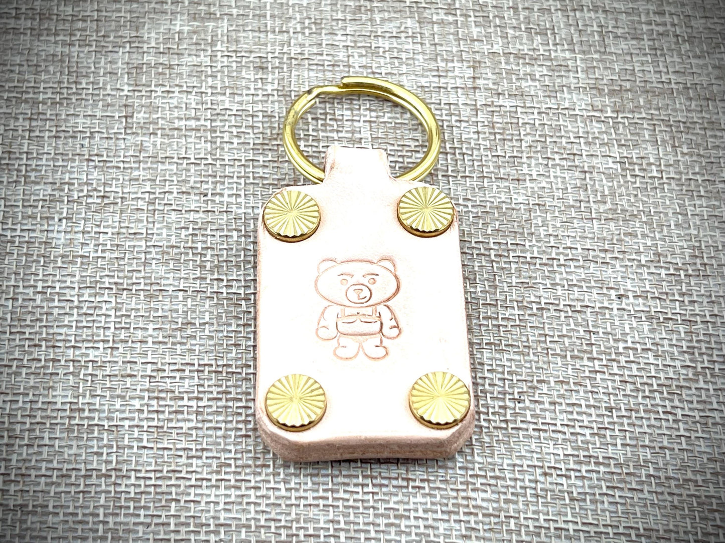 Keychain with teddy bear design and gold accents on a textured gray background