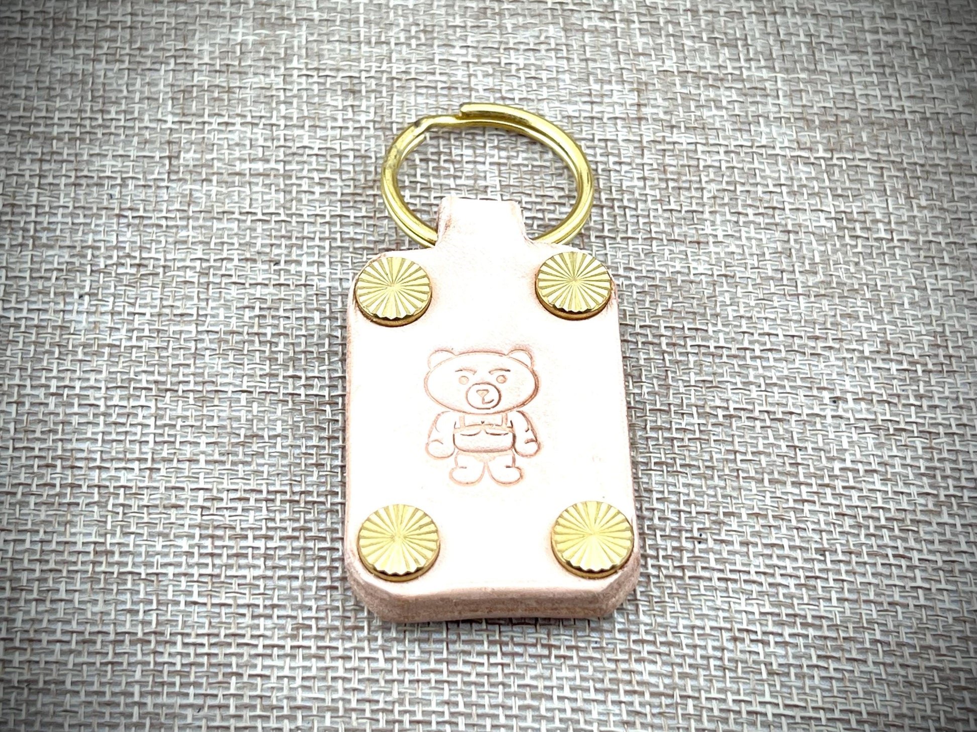 Keychain with teddy bear design and gold accents on a textured gray background
