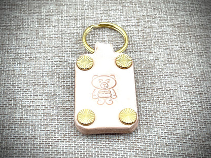 Keychain with teddy bear design and gold accents on a textured gray background