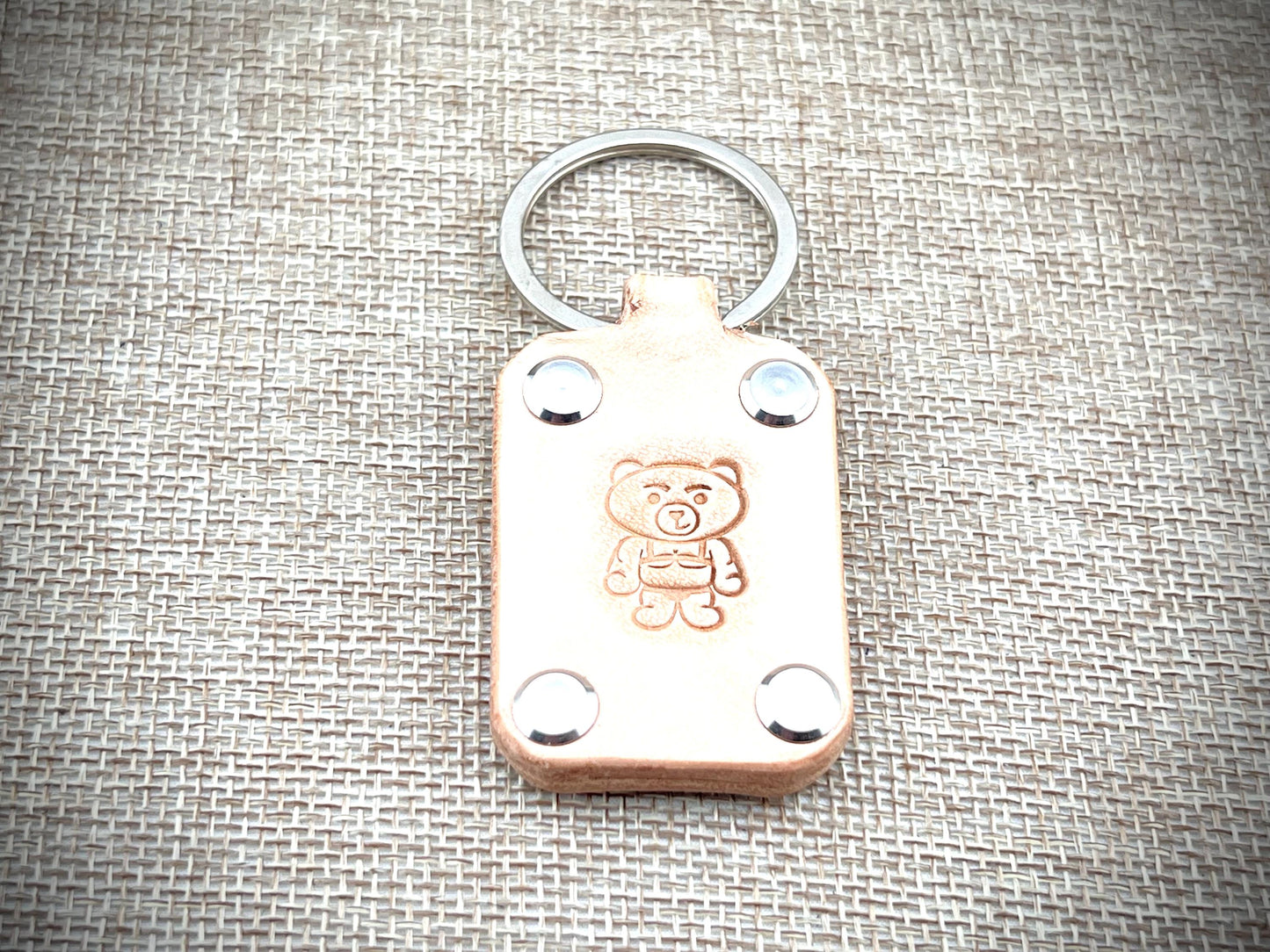 Leather keychain with teddy bear design on a textured fabric background