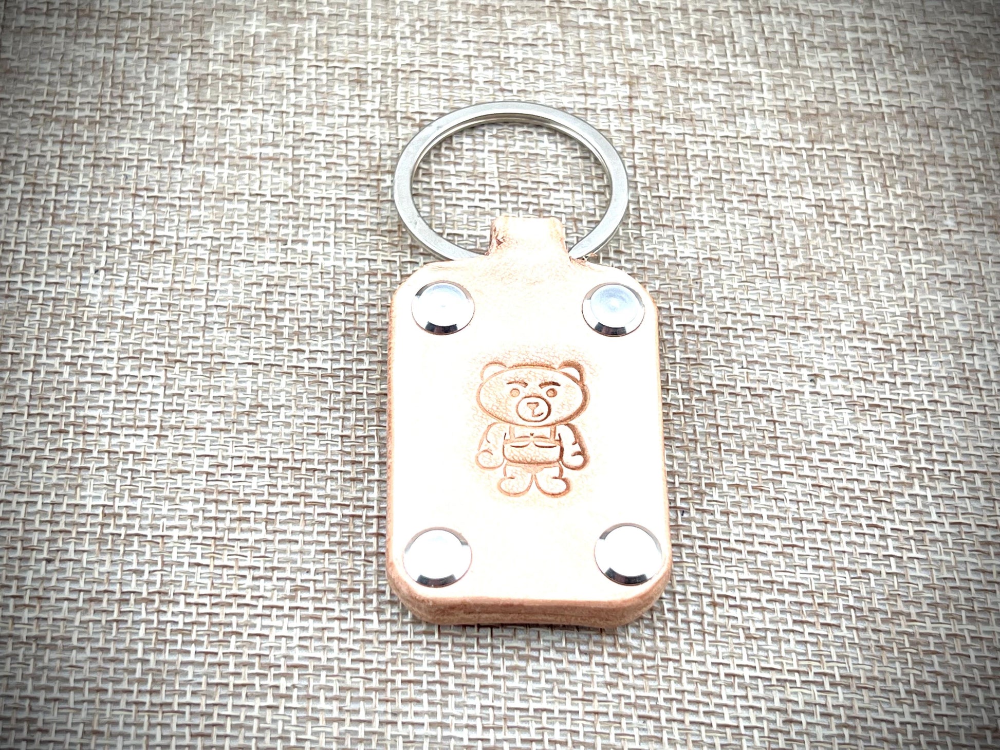 Leather keychain with teddy bear design on a textured fabric background