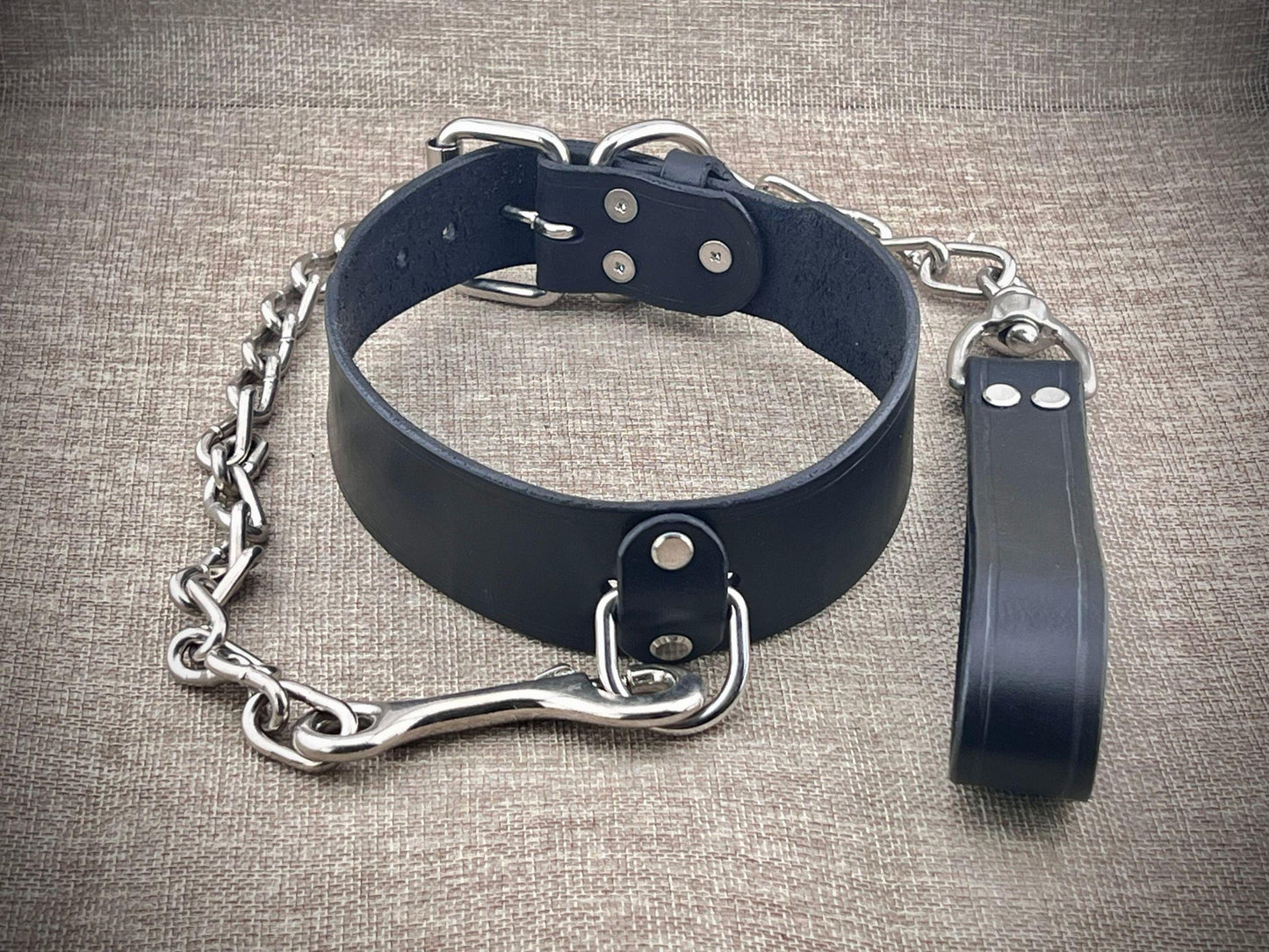 Black leather collar with chain and leash on a textured surface