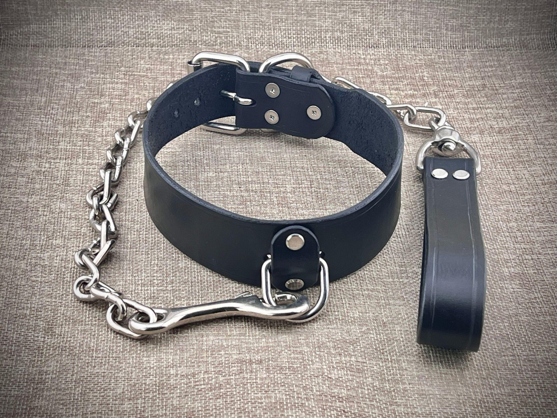 Black leather collar with chain and leash on a textured surface