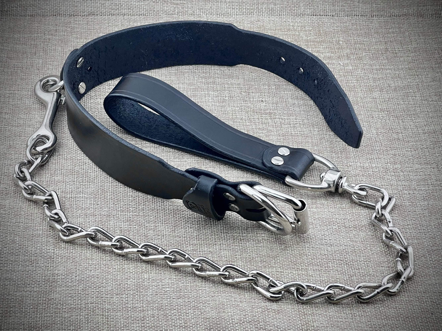 Black leather collar with steel chain on a textured gray background