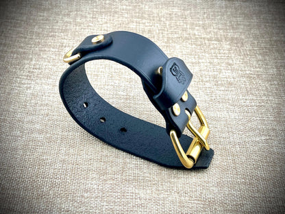 Black leather cuff with gold hardware on a textured gray background