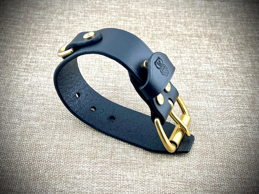 Black leather cuff with gold hardware on a textured gray background