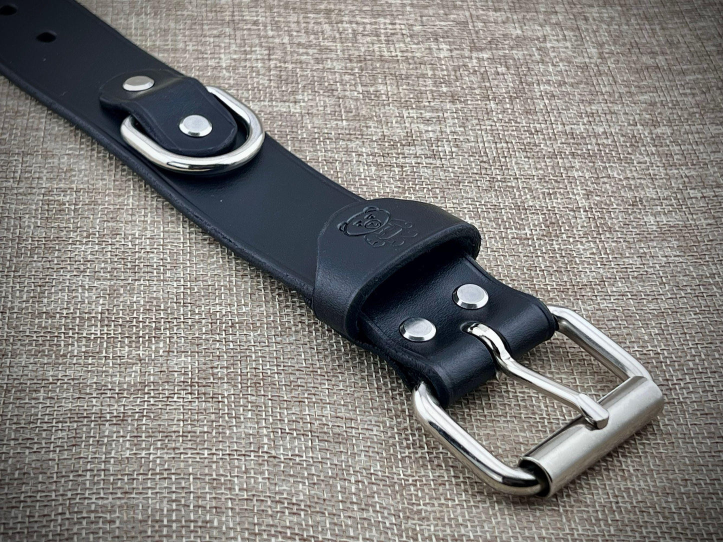 Black leather belt with silver buckle on a textured fabric background