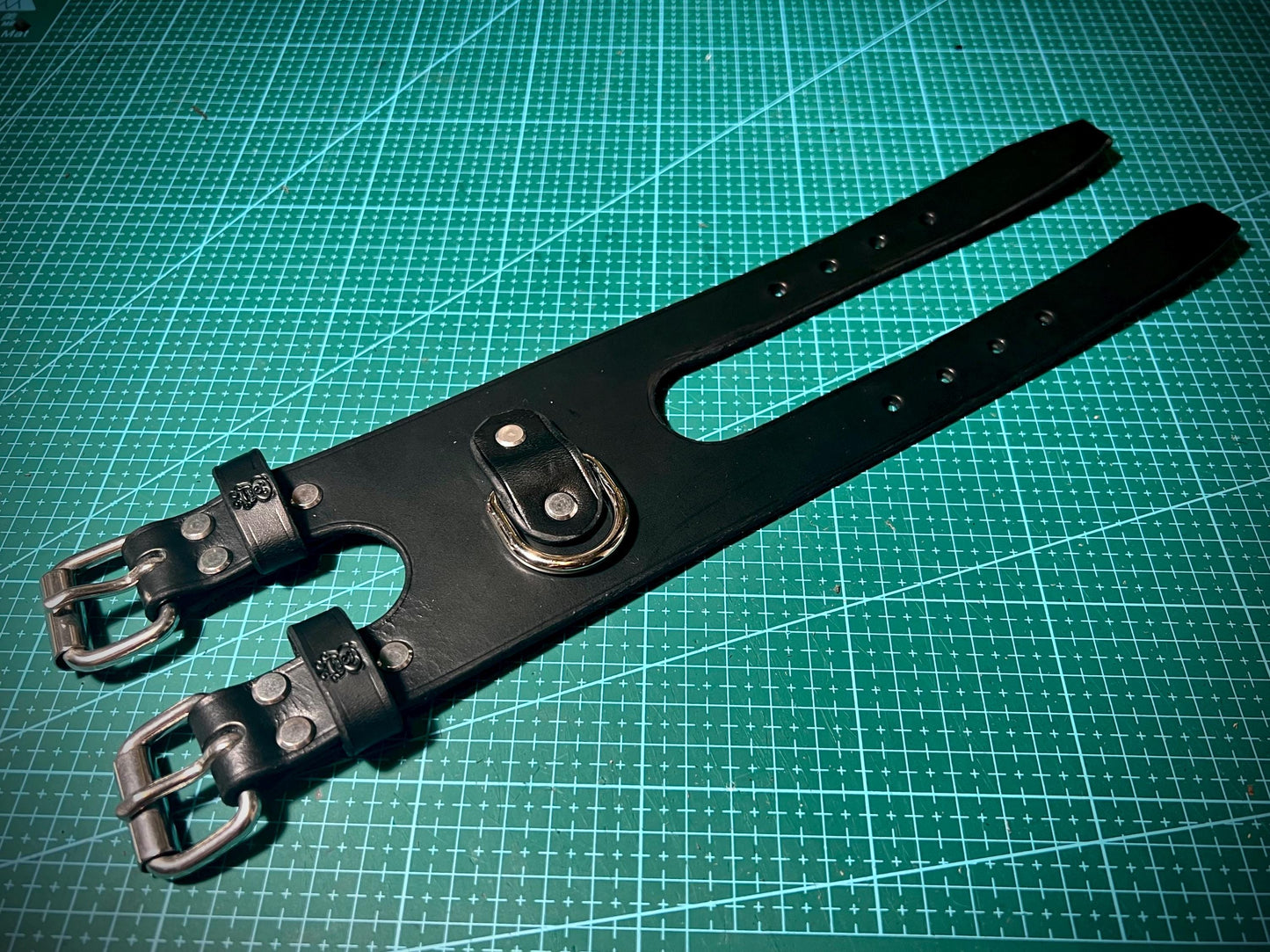 Black leather strap with steel buckles on a green cutting mat