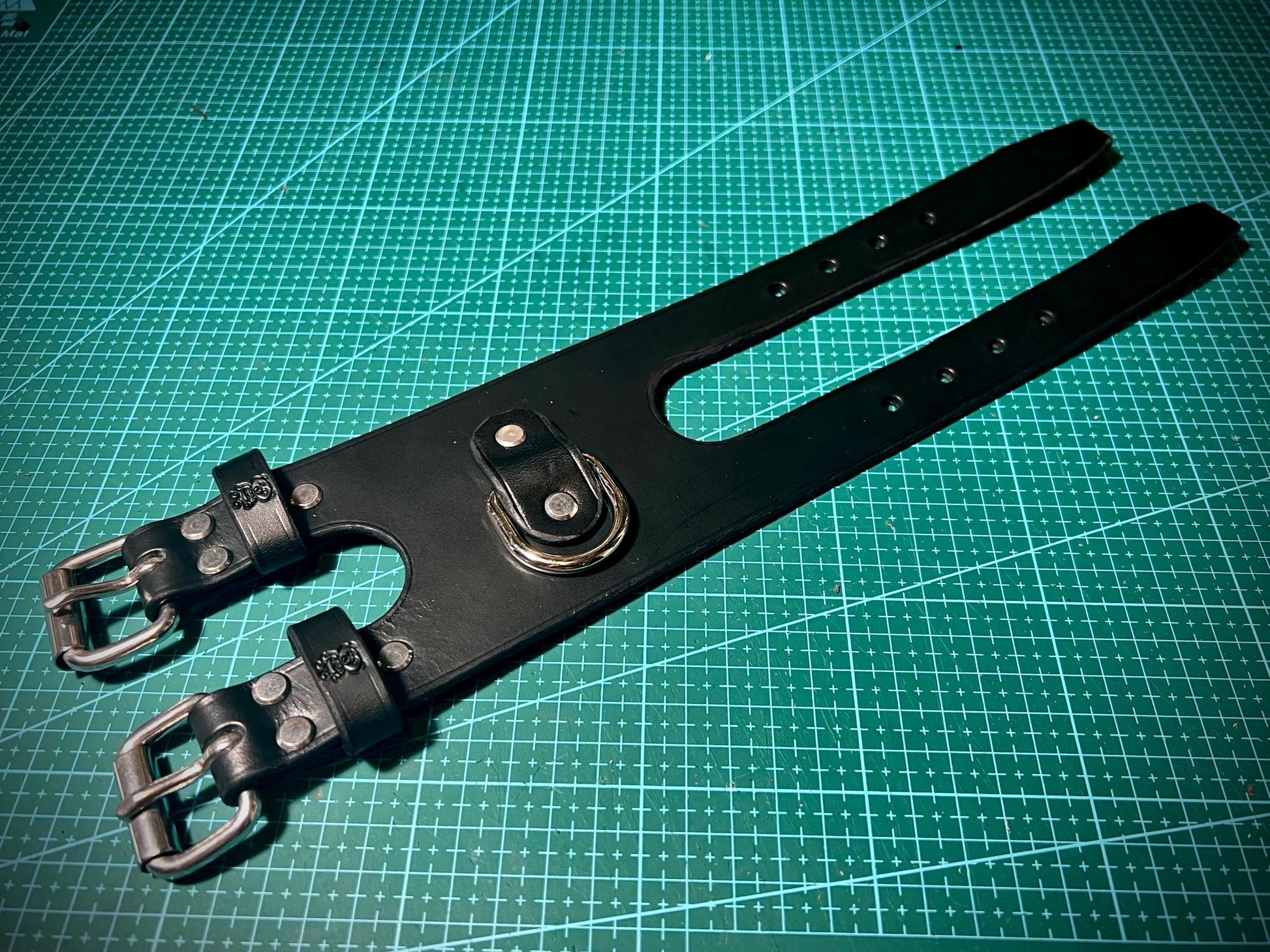 Black leather strap with steel buckles on a green cutting mat