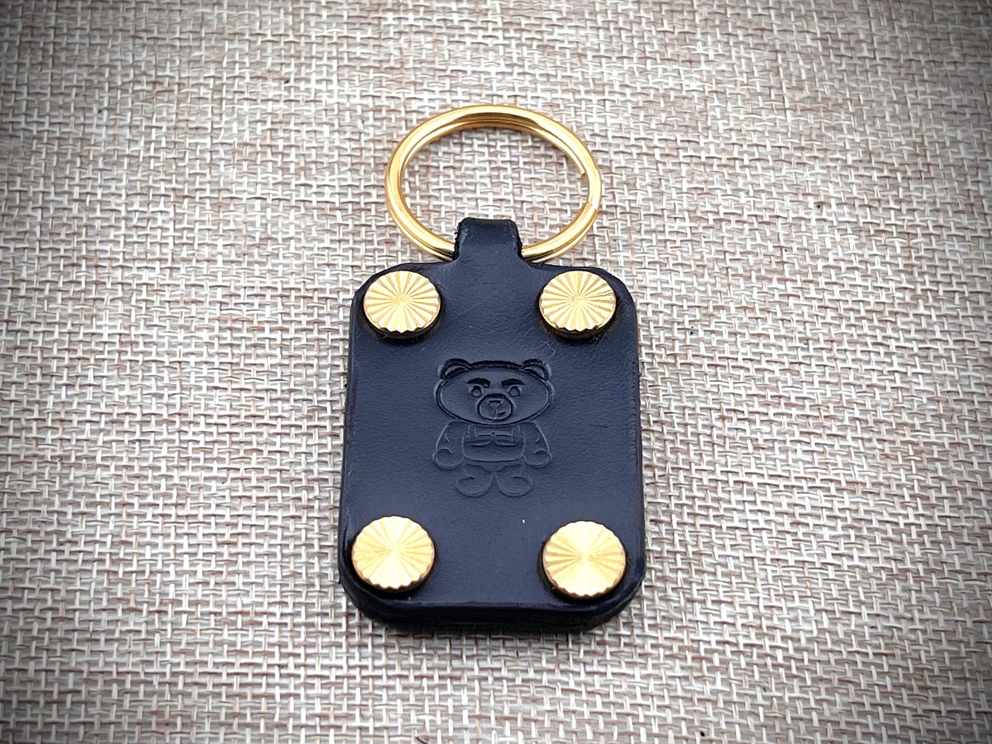 Black leather key fob with gold studs and a bear emblem on a textured gray background