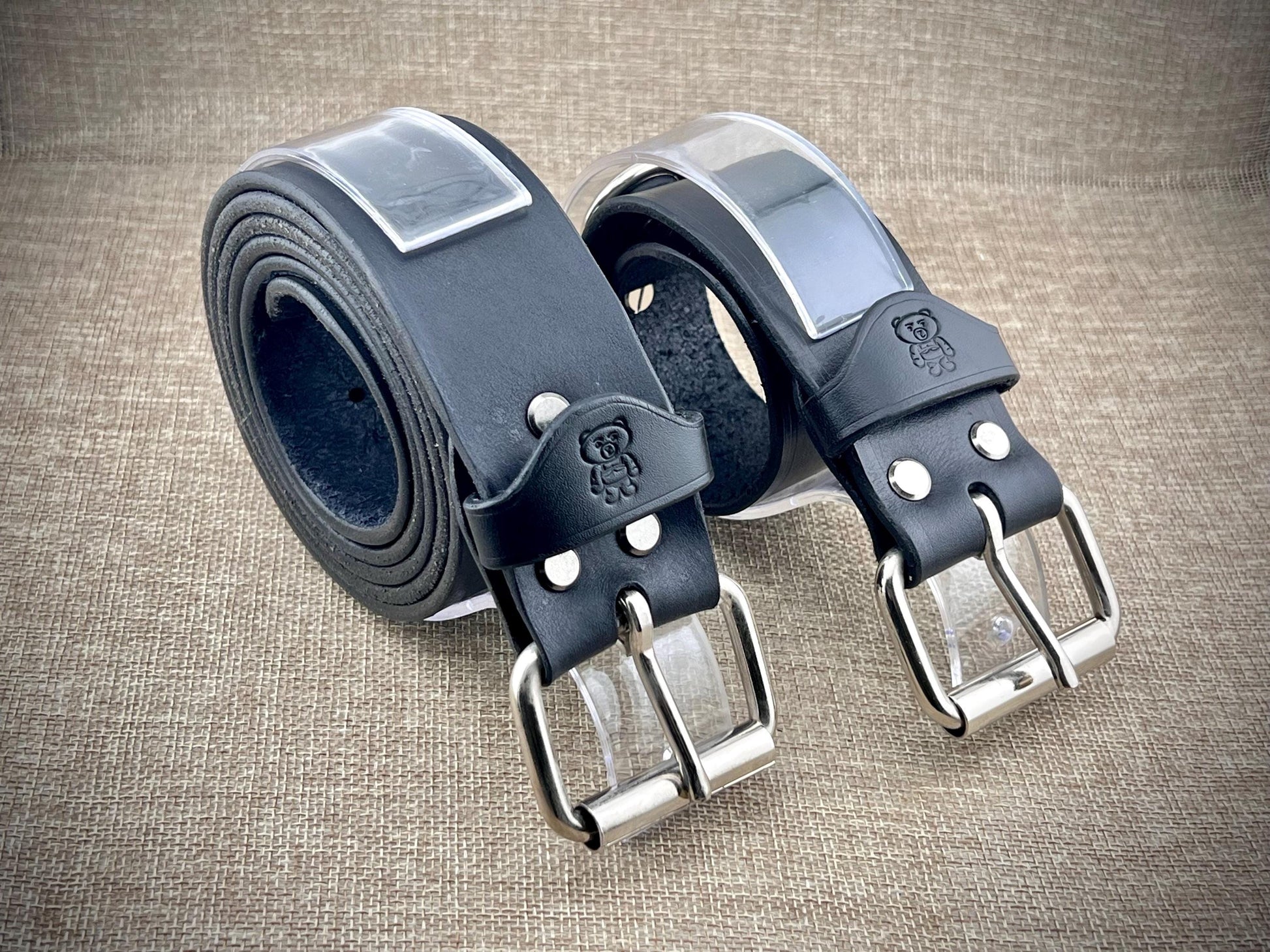 Two black leather belts with silver buckles on a textured brown background