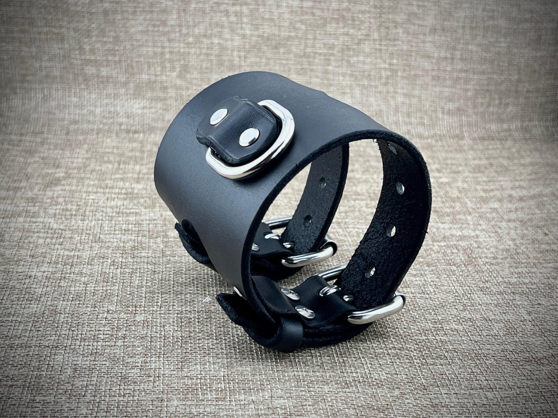 Black leather cuff with metal hardware on a textured gray background