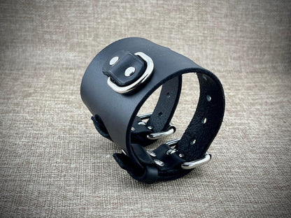 Black leather cuff with metal hardware on a textured gray background