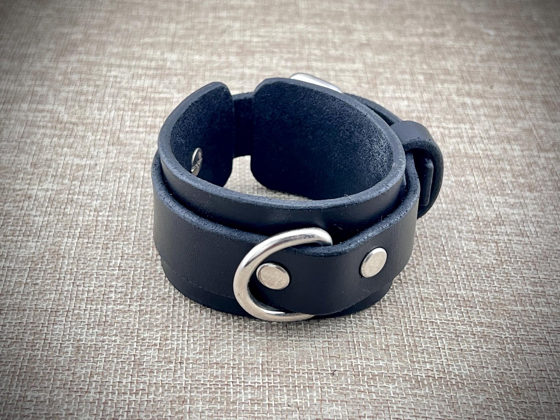 Black leather bracelet with silver hardware on a textured gray background