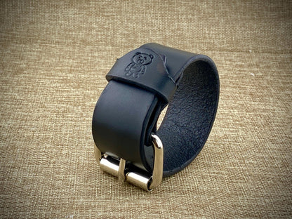 Black leather strap with metal buckle on a textured beige background