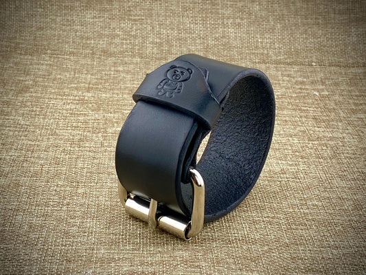 Black leather strap with metal buckle on a textured beige background