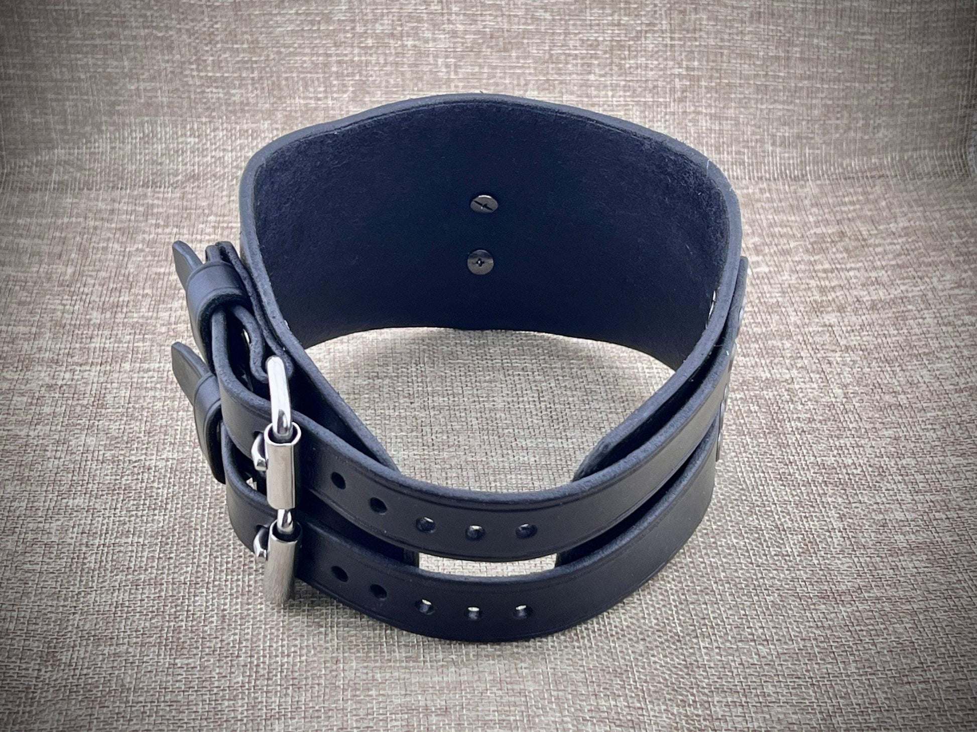 Black leather collar with metal clasp on a textured gray background