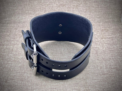 Black leather collar with metal clasp on a textured gray background
