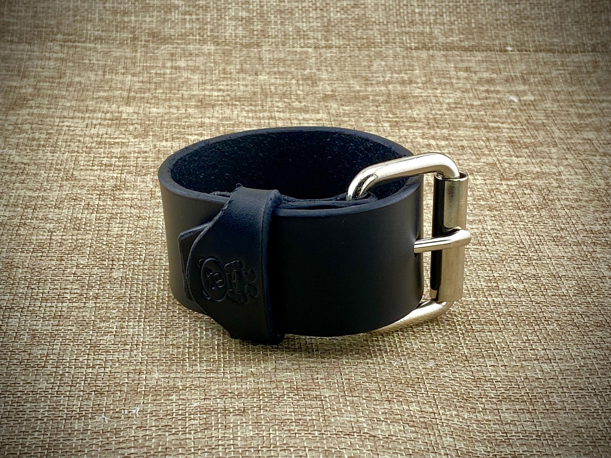 Black leather watch strap with silver buckle on a textured beige background