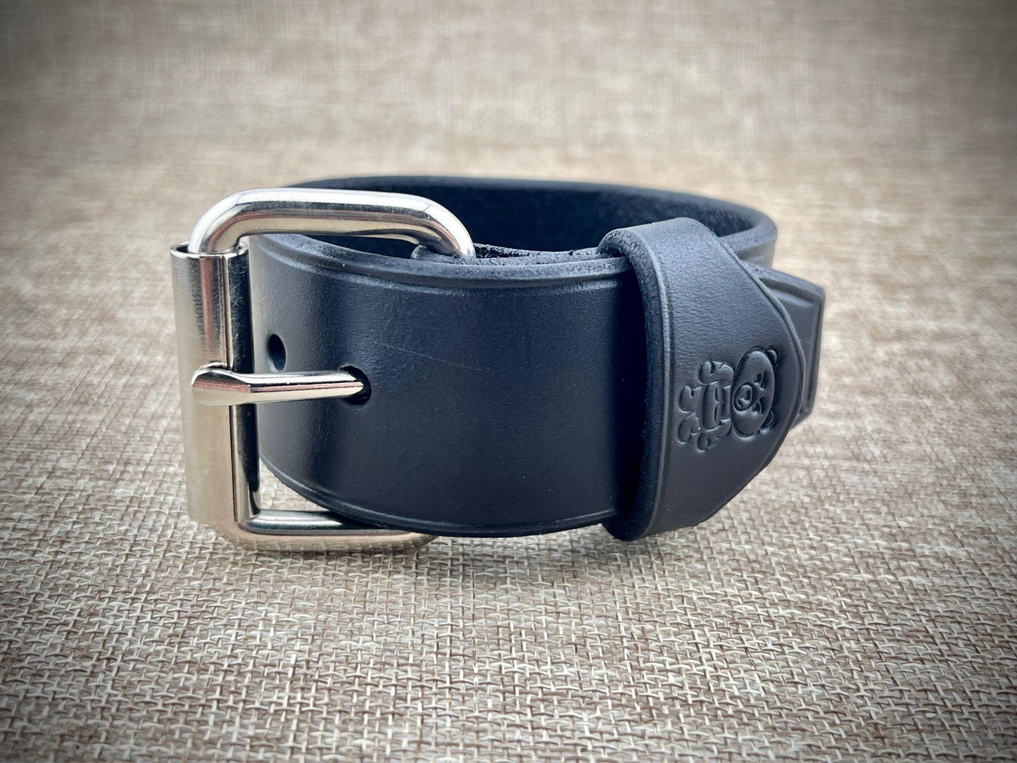 Black leather belt with silver buckle on a textured beige background