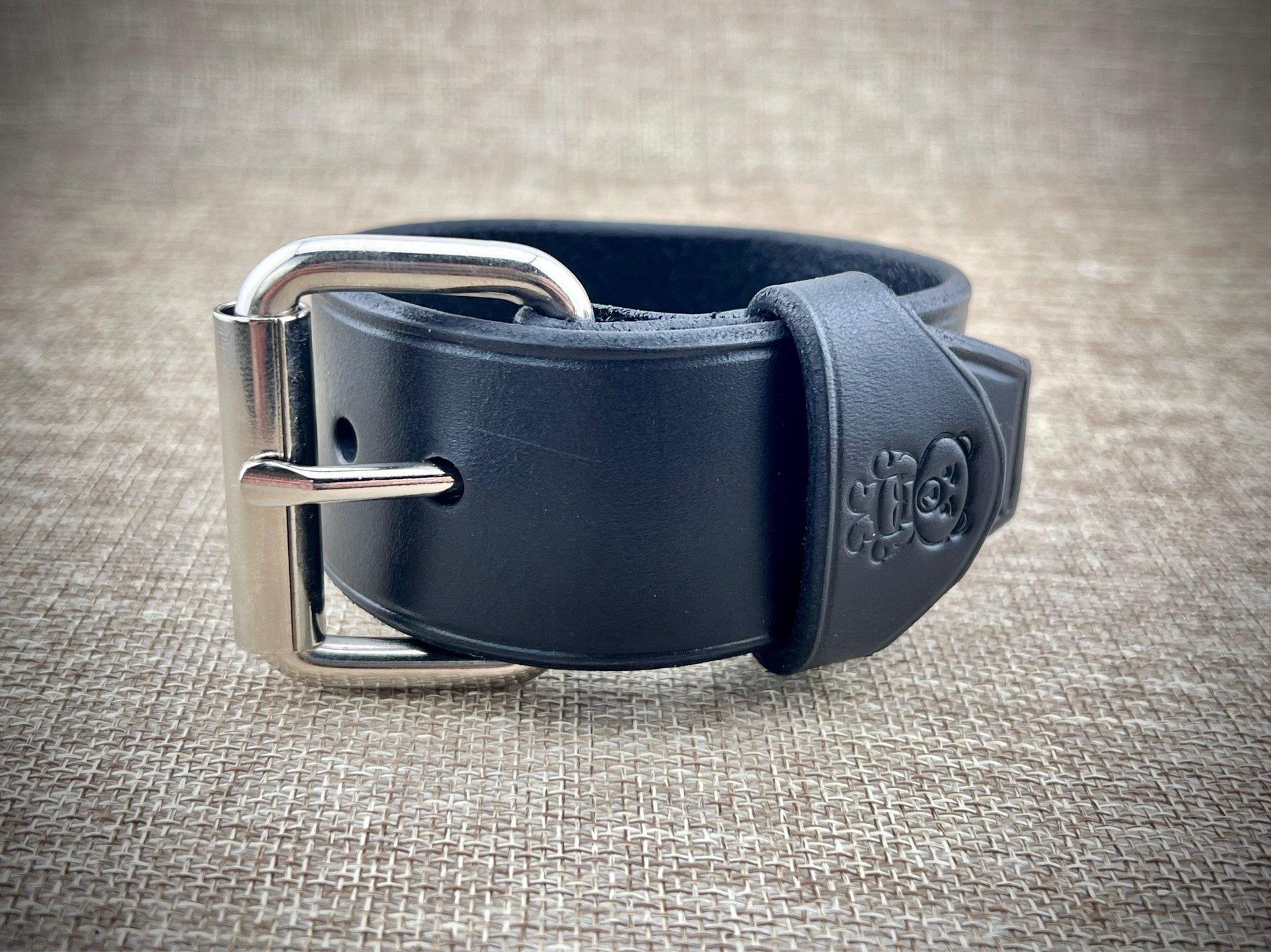 Black leather belt with silver buckle on a textured beige background