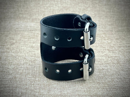 Black leather cuff with metal clasp on a textured beige background