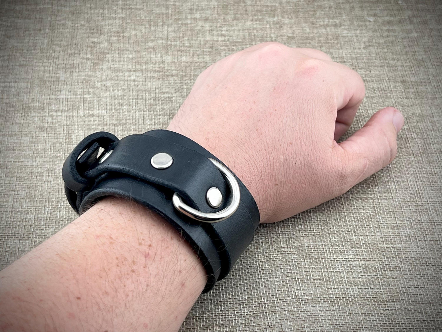 Black leather wristband with metal buckles on a textured surface