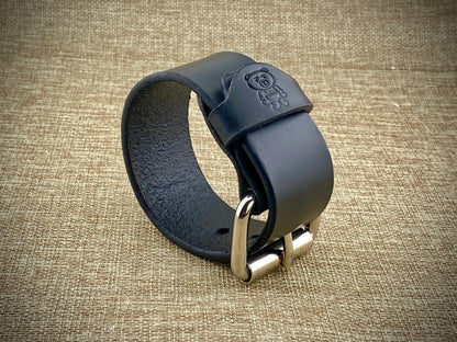 Black leather strap with metal buckle on a textured beige background