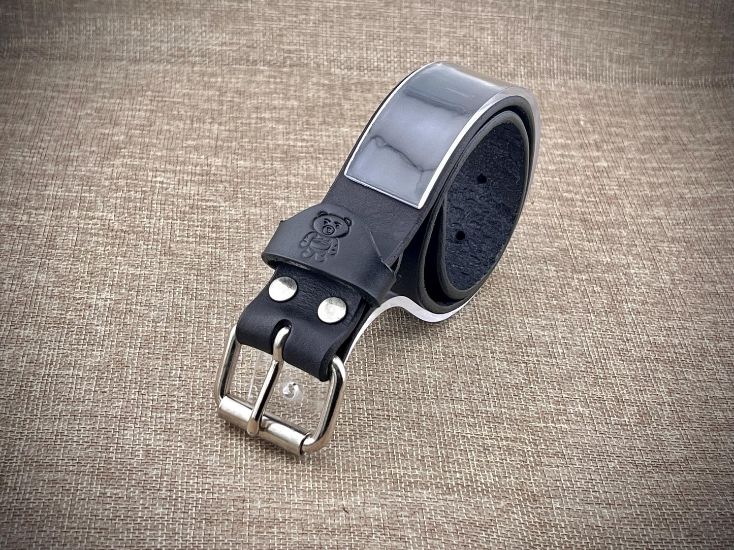 Black leather belt with silver buckle on a textured brown background