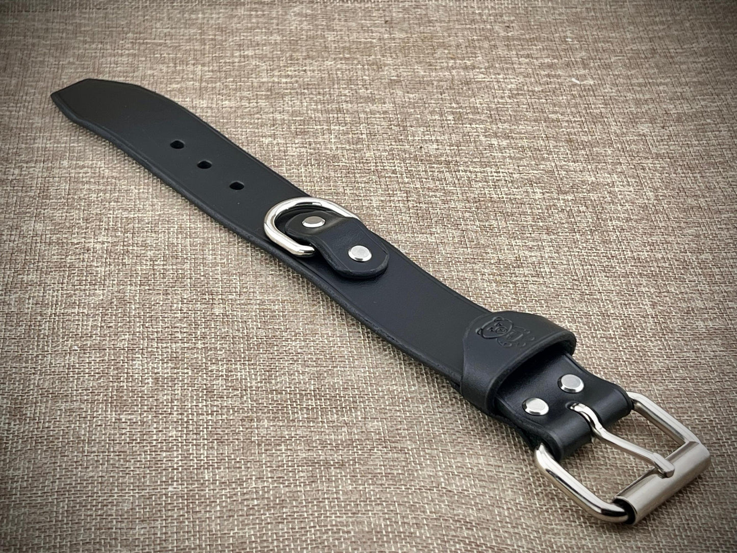 Black leather belt with silver buckle on a textured brown background