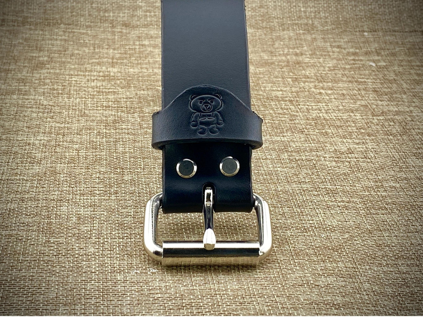 Black leather belt with silver buckle on a textured beige background