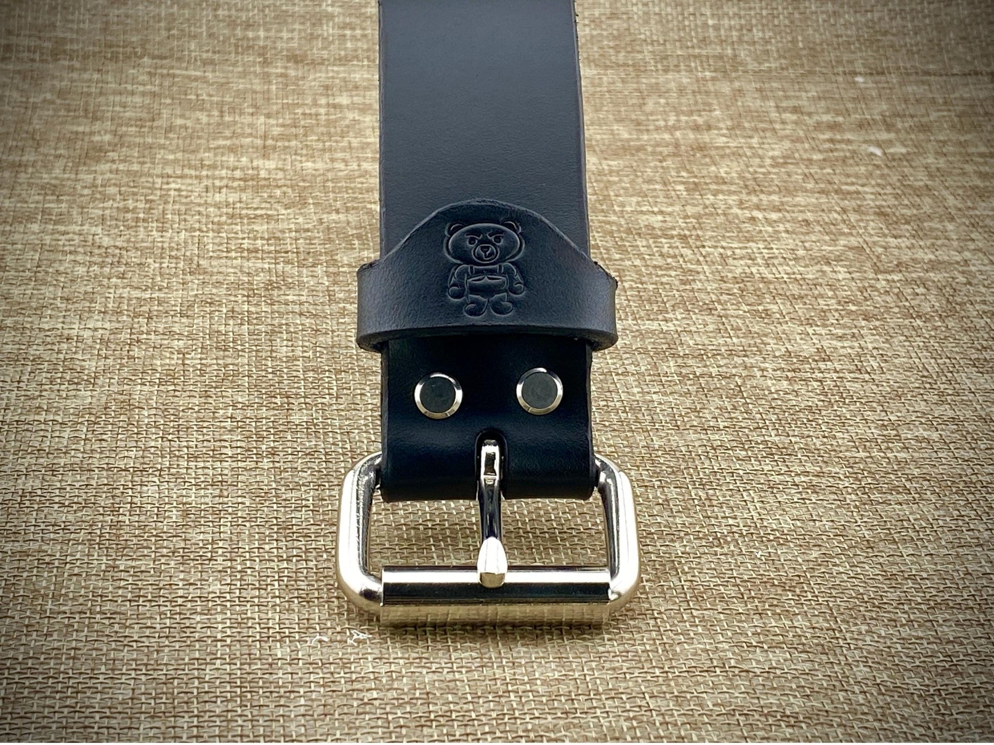 Black leather belt with silver buckle on a textured beige background