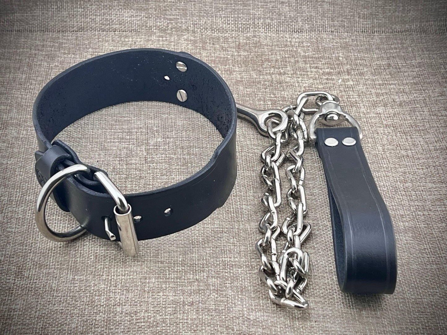 Black leather collar with metal chain on a textured gray background