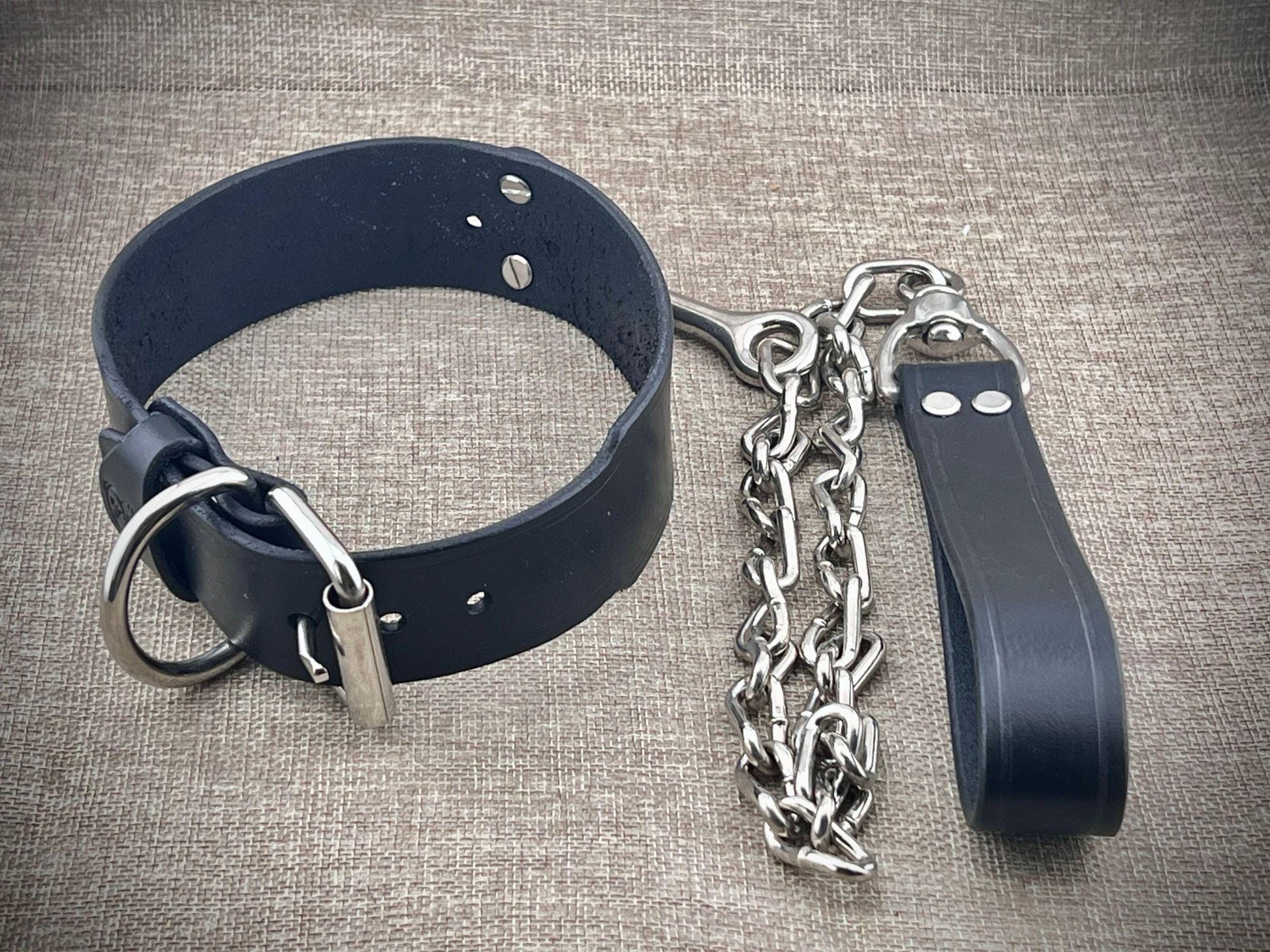 Black leather collar with metal chain on a textured gray background