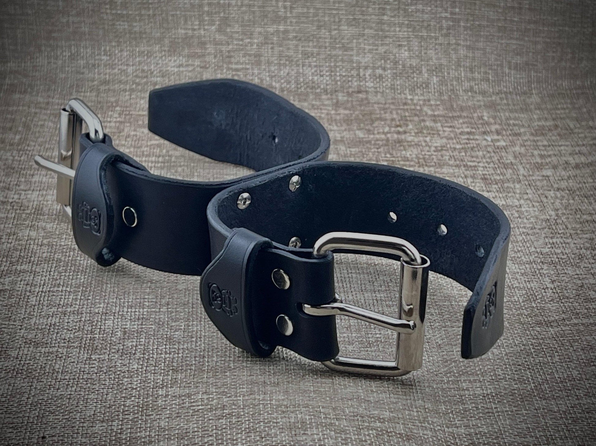 Two black leather bondage cuffs s with silver buckles on a textured gray background